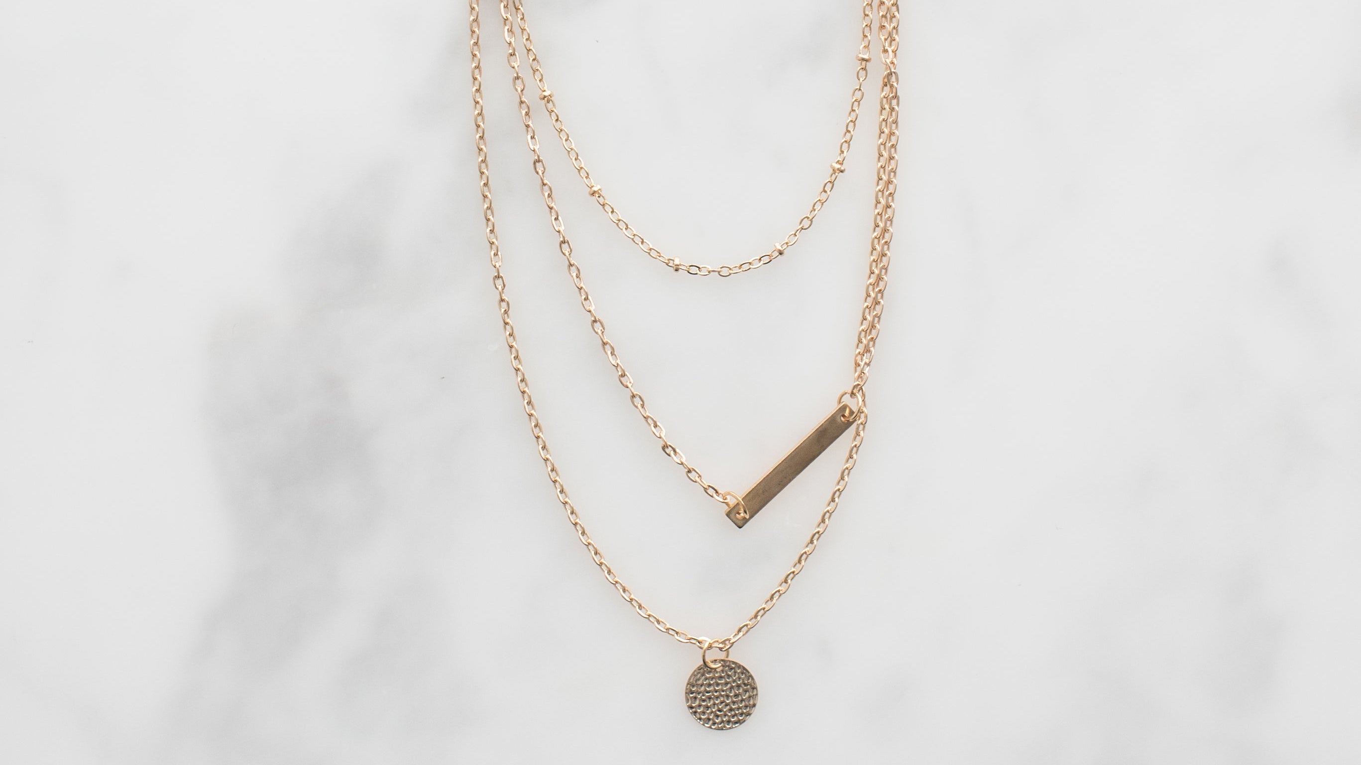 Three gold necklaces with different pendants on a light gray background