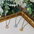 Three necklaces with round pendants on a textured surface with plants in the background