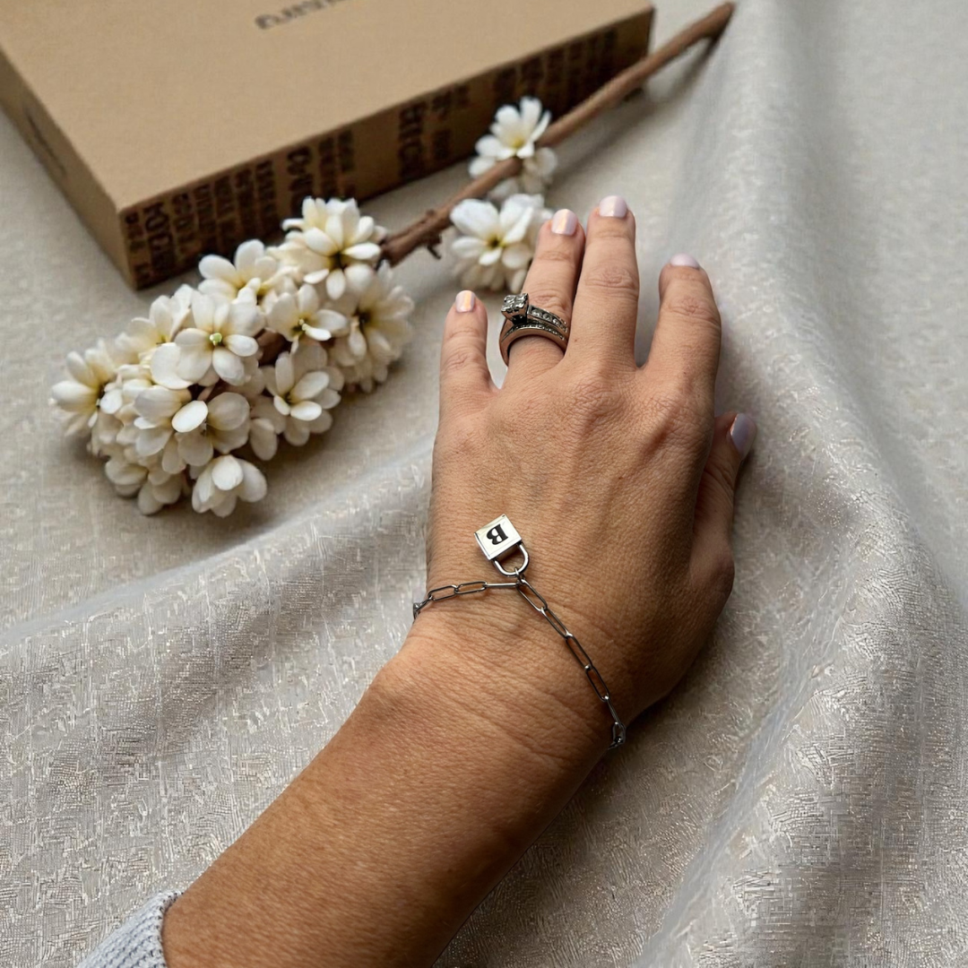 Engraved silver lock bracelet with initial lock charm worn on a wrist.