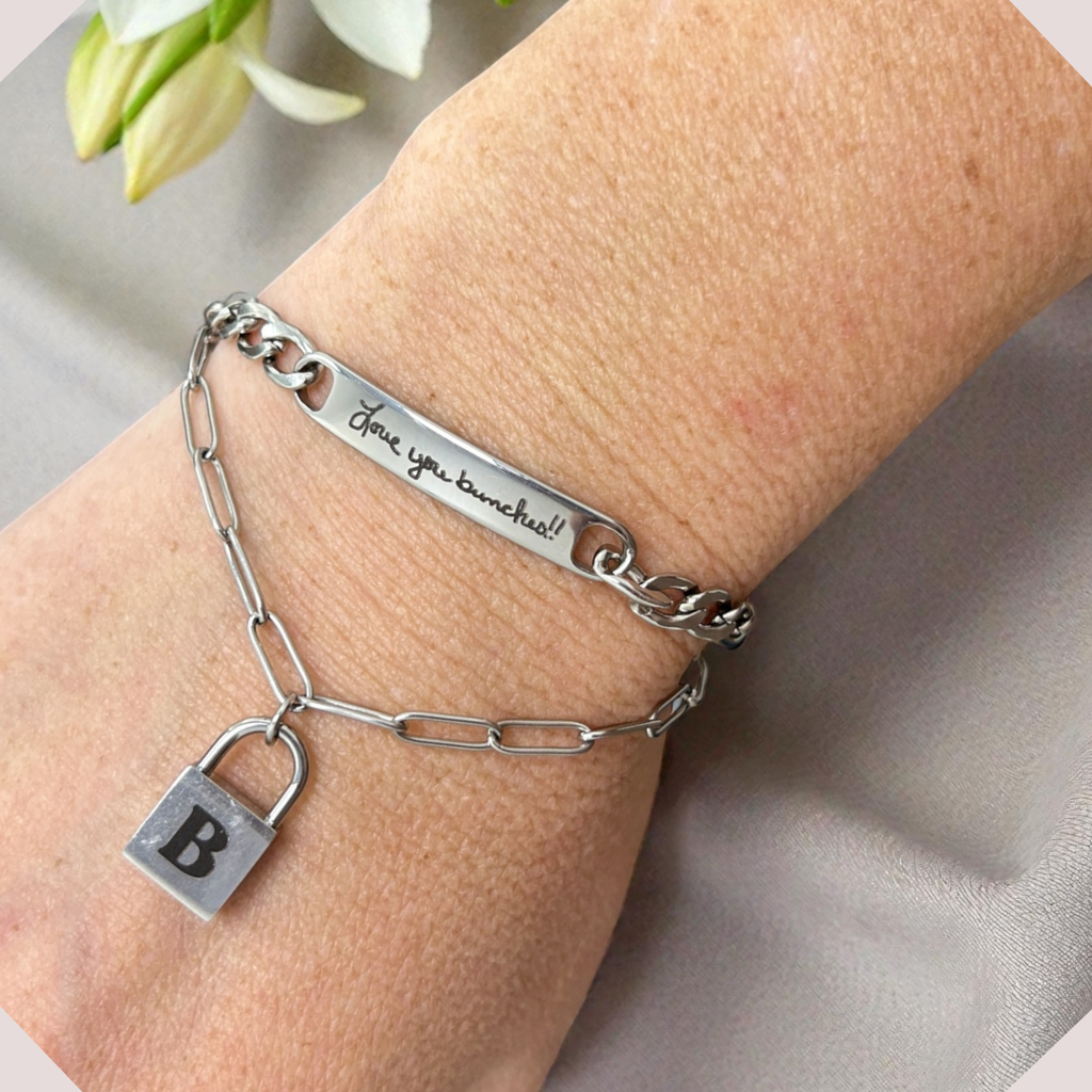 Silver chain bracelet with a lock charm on a wrist, against a neutral background.