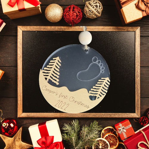 Baby's first Christmas ornament. A snowy scene with a baby foot outlined with stars in the sky.