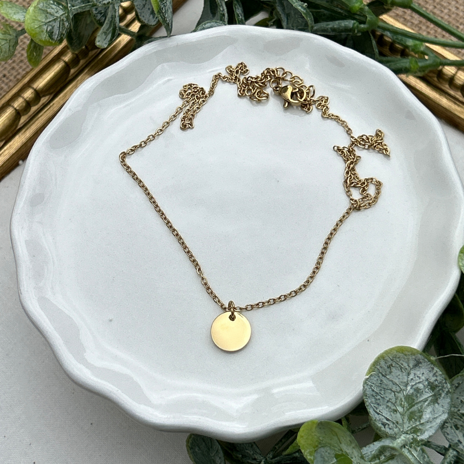 Gold necklace on a white dish with greenery in the background