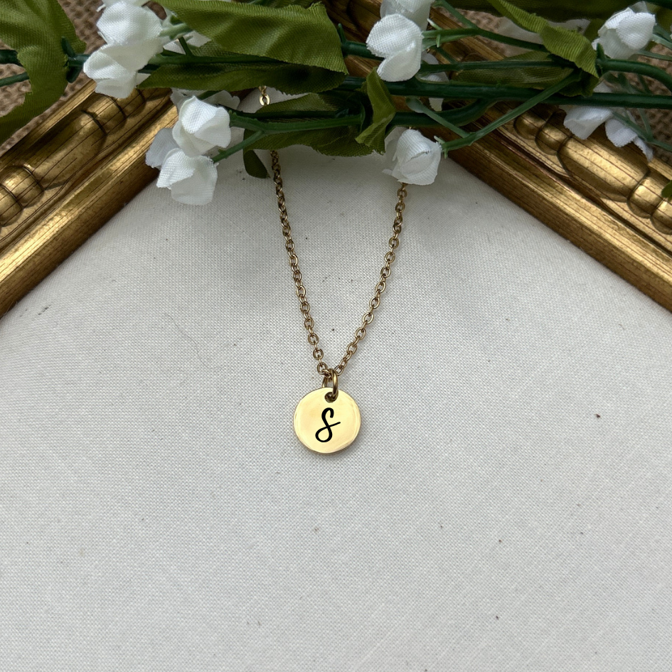 Gold necklace with a round pendant on a light gray surface with floral decorations.