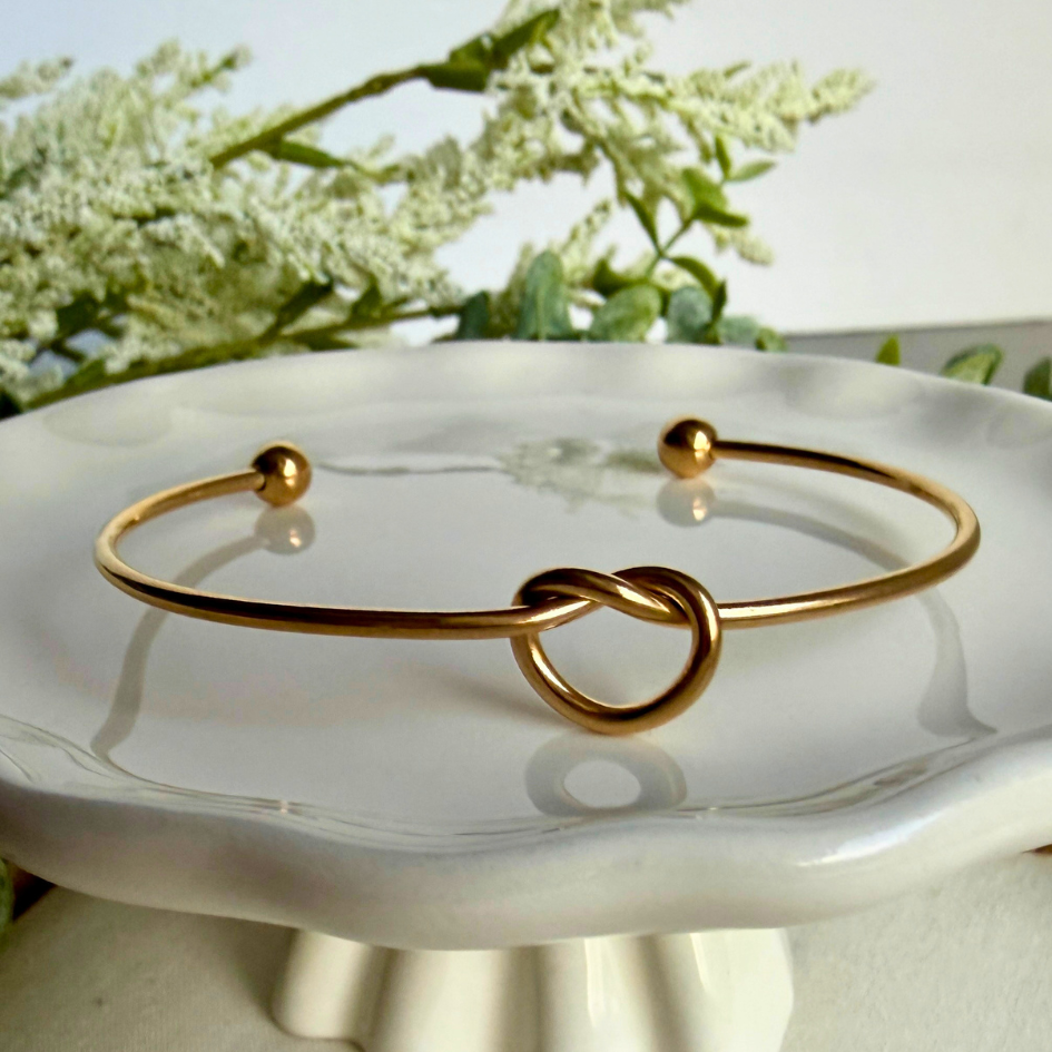 Gold bracelet with a knot design on a white dish with flowers in the background