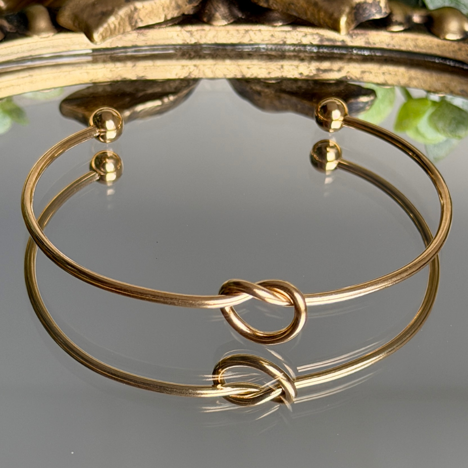 Gold bracelet with a knot design on a reflective surface