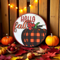 Decorative sign with 'Hello fall' text and plaid pumpkin design, surrounded by pumpkins and leaves.
