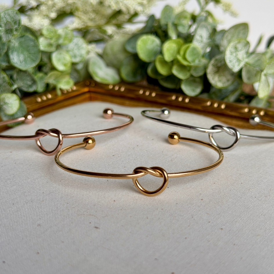 Gold and silver bracelets on a white surface with greenery in the background