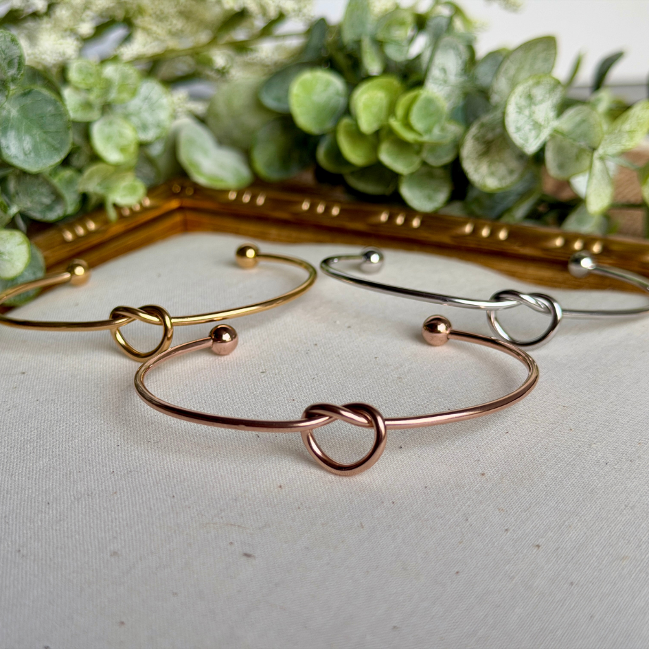 Three gold and rose gold bracelets on a white surface with green foliage in the background