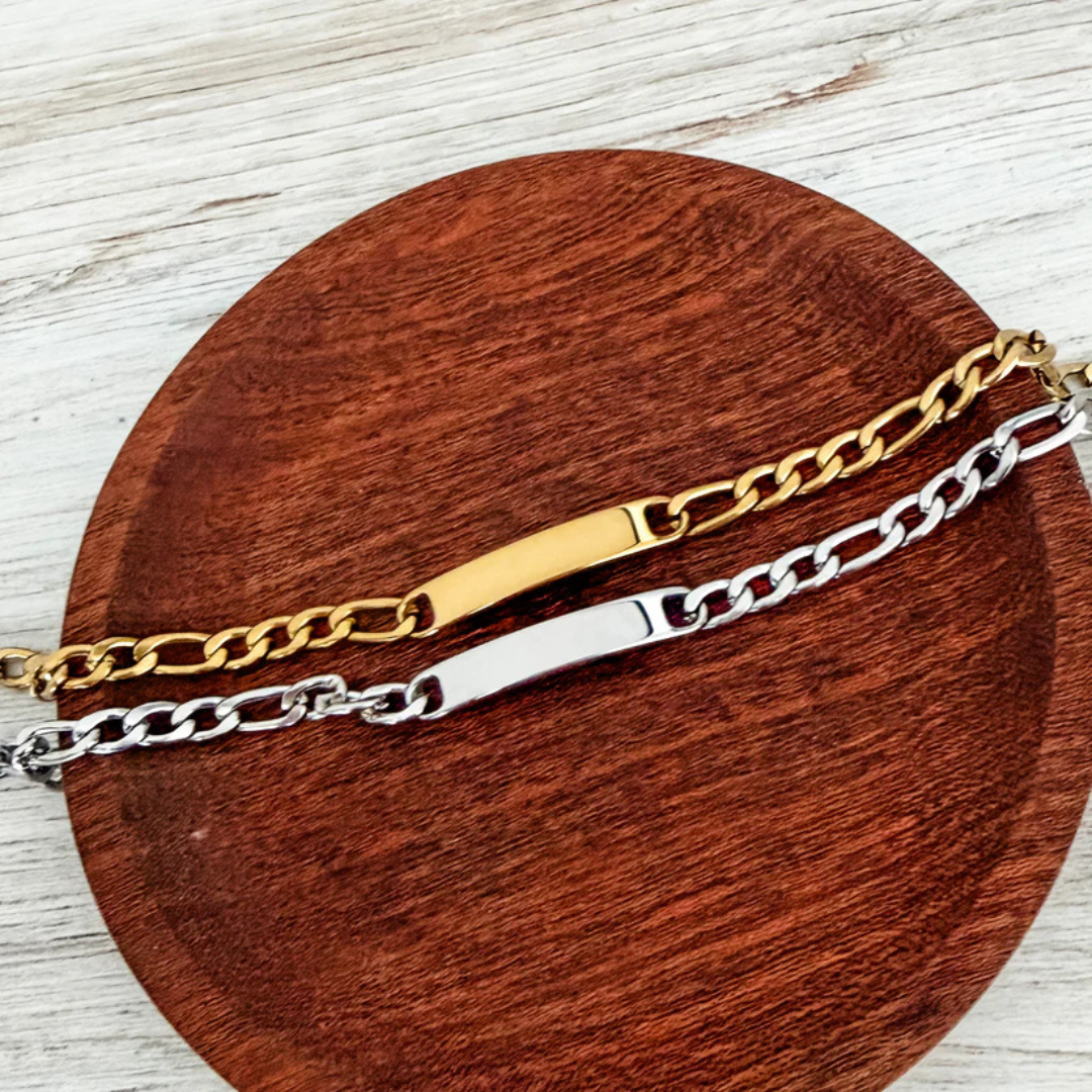 Two chain bracelets, one gold and one silver, on a wooden surface.