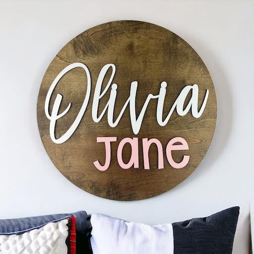 Dark wook round backer with the baby name cut out and painted in the colors that match the baby's nursery.