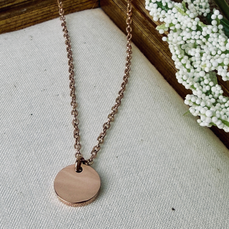 Rose gold necklace with a round pendant on a textured surface with white flowers in the background