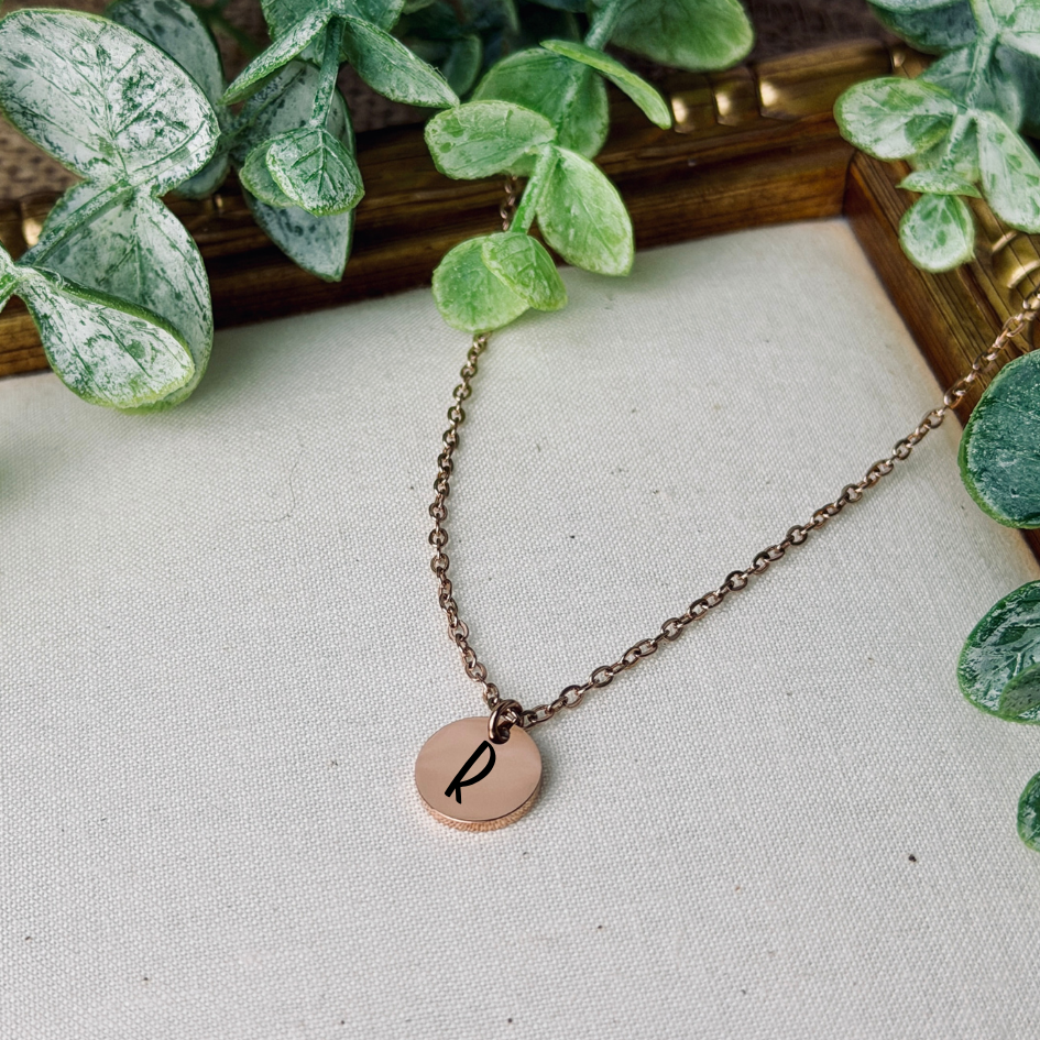 Necklace with a round pendant featuring a letter 'P' on a light surface with green leaves in the background.