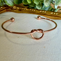 Rose gold knot bracelet on a light fabric surface with a decorative mirror in the background.