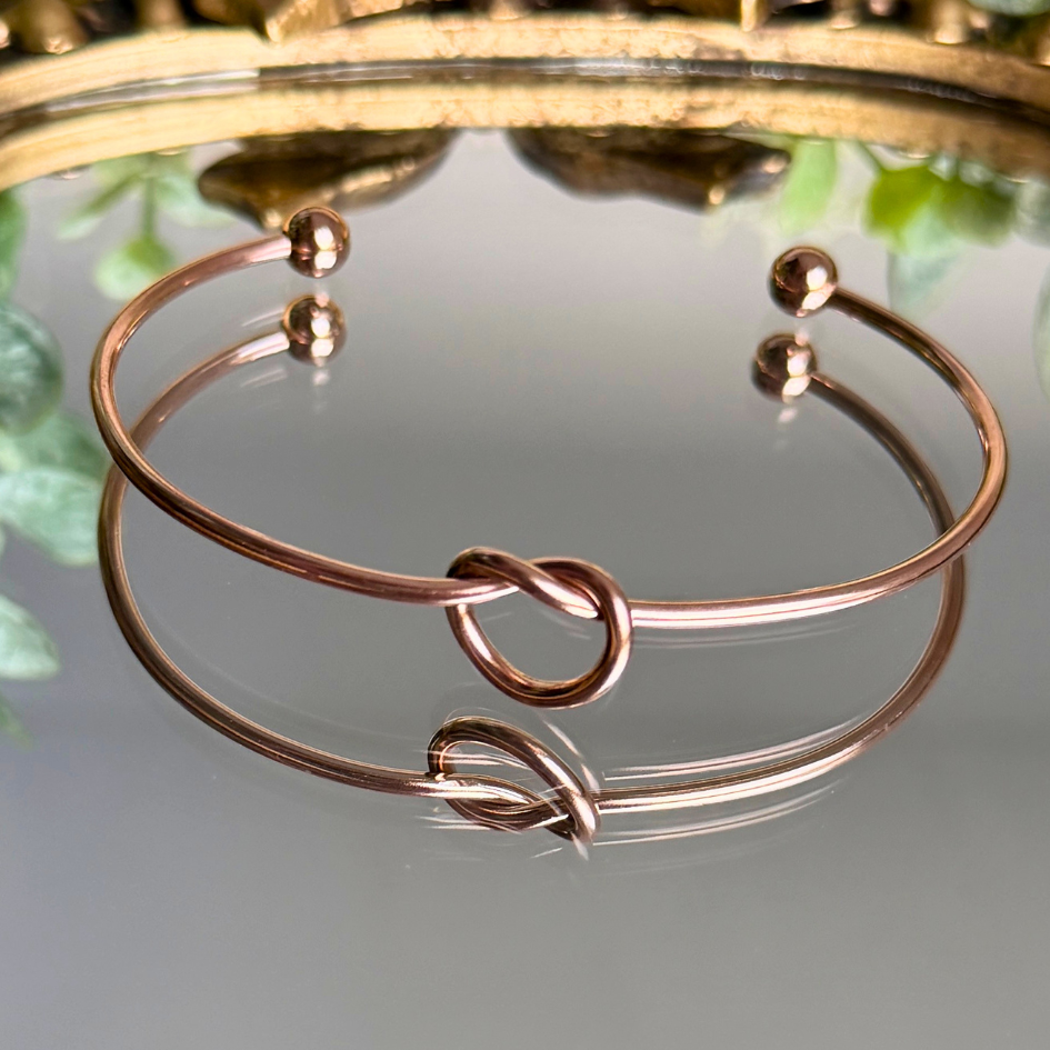 Rose gold bracelet with knot design on a reflective surface