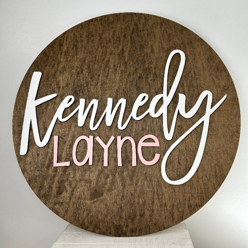 Dark wook round backer with the baby name cut out and painted in the colors that match the baby's nursery.