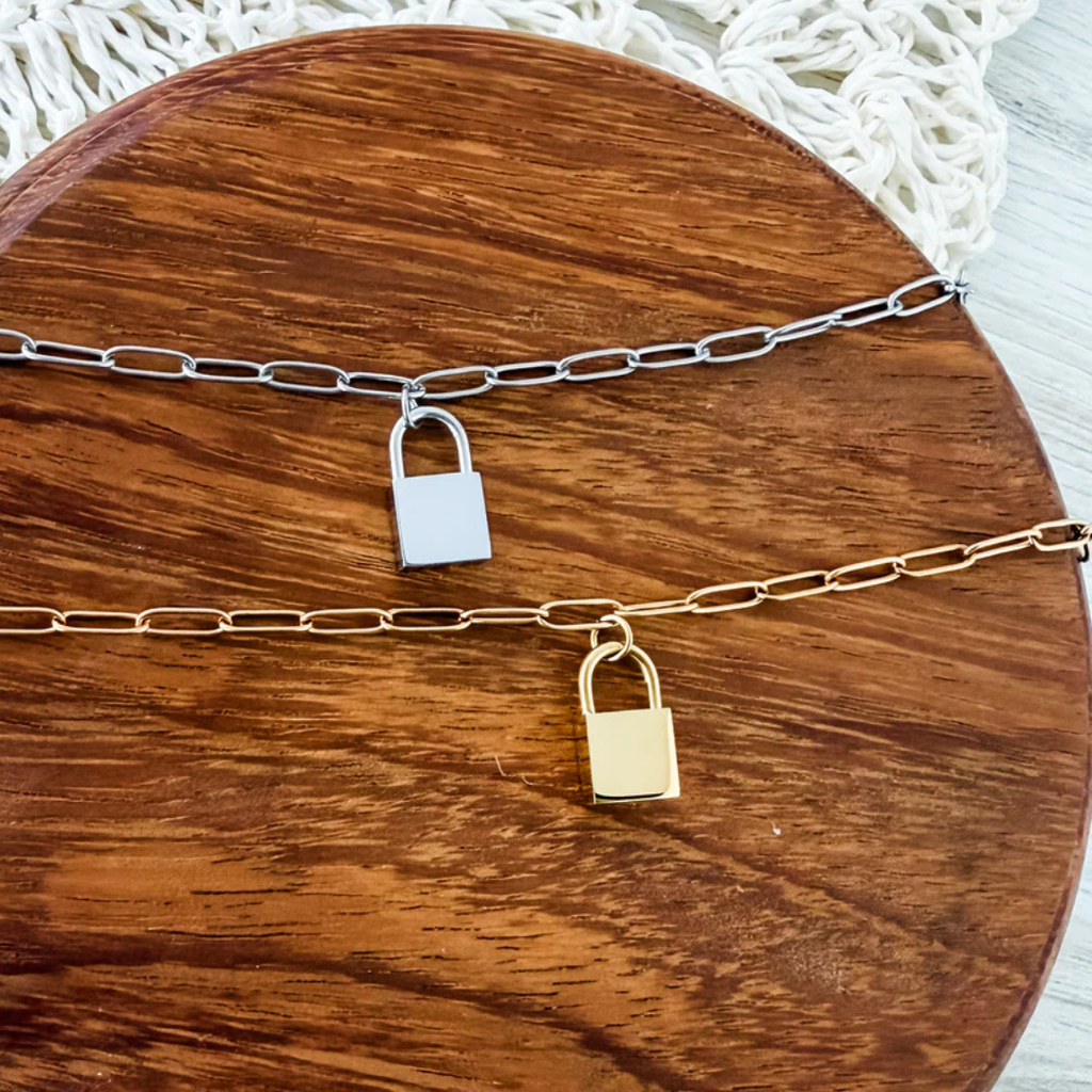 Silver and gold lock charm bracelets side by side unengraved on a wooden surface.