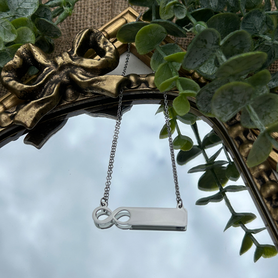 Silver necklace with an infinity symbol pendant hanging from a decorative frame with greenery.