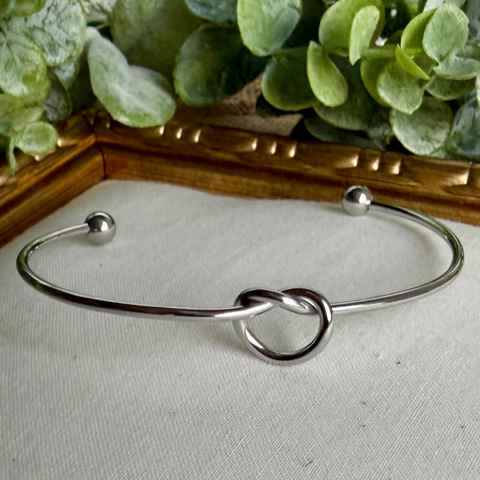 Silver knot bracelet on a light fabric background with green leaves in the background