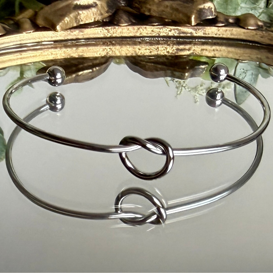 Silver bracelet with a knot design on a reflective surface