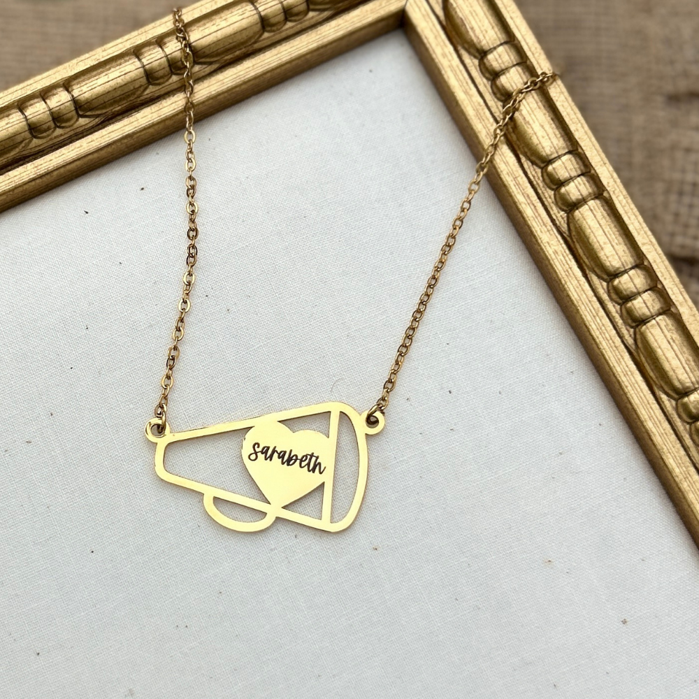 Gold necklace with a heart-shaped pendant and 'Saraeath' engraving on a light gray background.