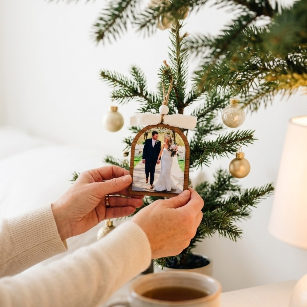 Person holding a Christmas ornament with a wedding photo in front of a decorated tree.