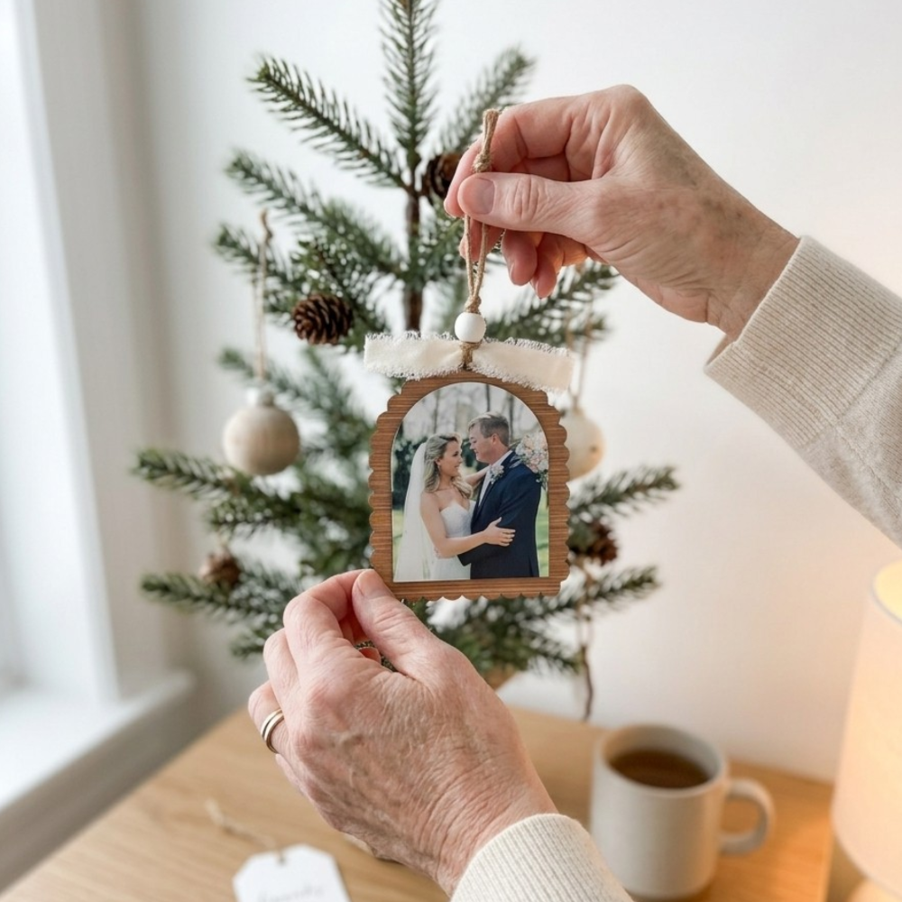 Hand holding a wooden ornament with a photo of a couple in front of a Christmas tree.