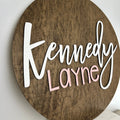 Dark wook round backer with the baby name cut out and painted in the colors that match the baby's nursery.